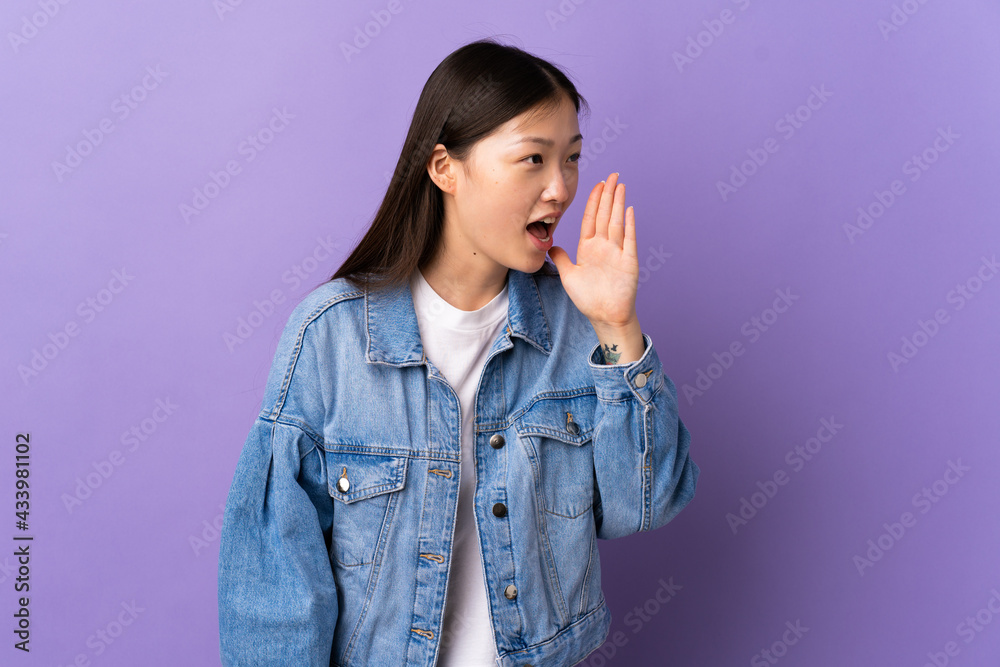 Young Chinese girl over isolated purple background shouting with mouth wide open to the side Young Chinese girl over isolated purple background shouting with mouth wide open to the side