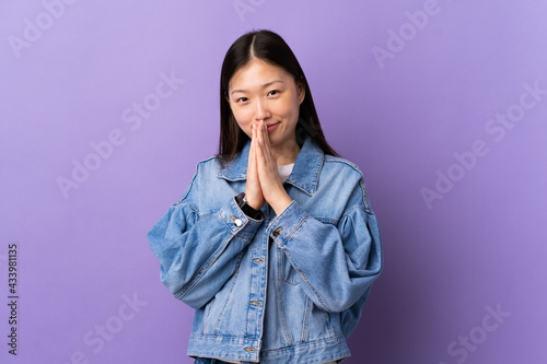 Young Chinese girl over isolated purple background keeps palm together. Person asks for something