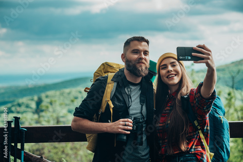 Couple of young hikers taking selfie with a smartphone while wearing camping backpacks