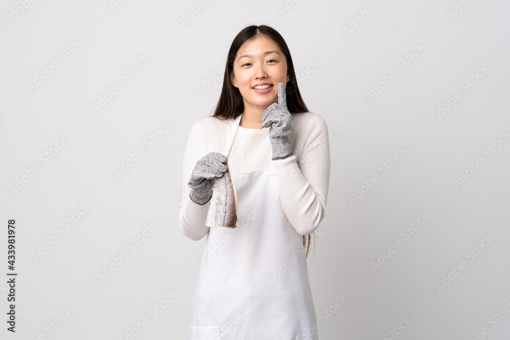 Chinese fishmonger wearing an apron and holding a raw fish over isolated white background smiling with a happy and pleasant expression Chinese fishmonger wearing an apron and holding a raw fish over isolated white background smiling with a happy and pleasant expression