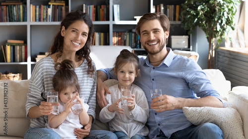 Portrait of happy young Caucasian family with two small daughters recommend drinking clear clean still water. Smiling parents with little kids give recommendation to healthy lifestyle and hydration. photo