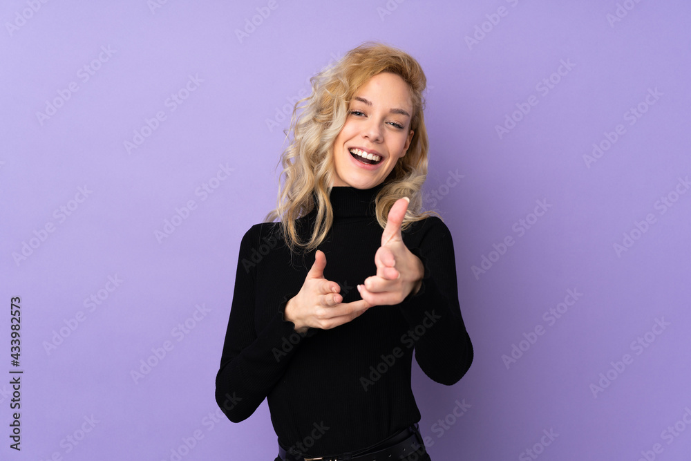 Young blonde woman isolated on purple background pointing to the front and smiling Young blonde woman isolated on purple background pointing to the front and smiling