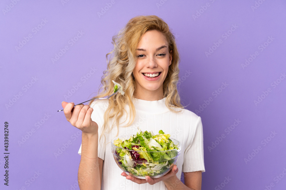 Young blonde woman holding salad isolated on purple background Young blonde woman holding salad isolated on purple background