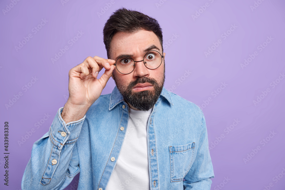 Φωτογραφία Indoor shot of handsome surprised adult man with thick beard looks attentively t