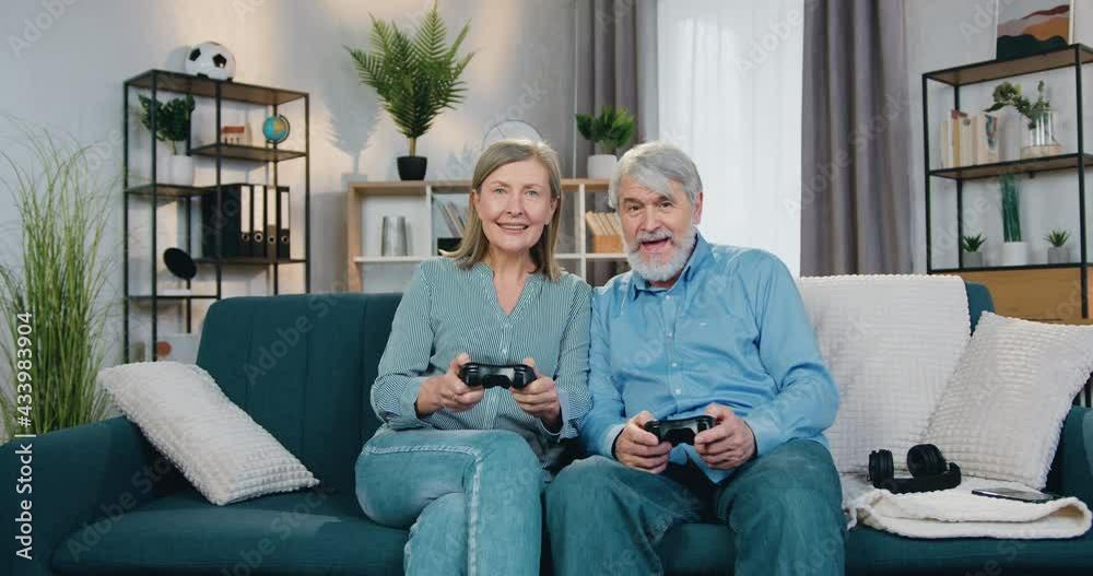 Excited senior couple playing games using wireless joysticks Excited senior couple playing games using wireless joysticks