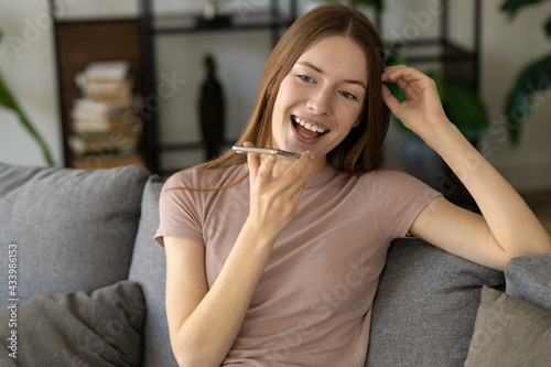 Happy caucasian millennial woman caller talking on the phone at home in living room. Cheerful girl enjoys pleasant mobile conversation on the phone sitting on the couch at home