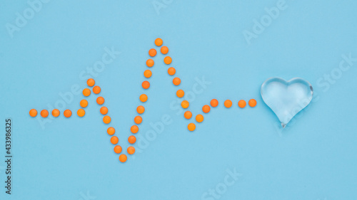 A cardiogram of pills resting on a glass heart. Flat lay.