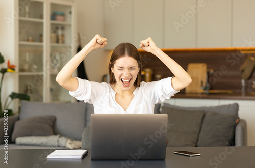 Excited happy caucasian woman sitting at the table at home feel euphoric win online lottery or get mail at laptop with great news
