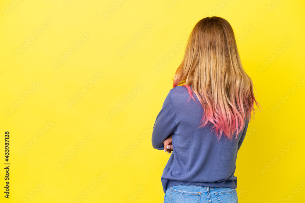 Young woman over isolated yellow background in back position Young woman over isolated yellow background in back position