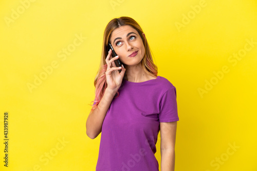 Young woman using mobile phone over isolated yellow background and looking up © luismolinero