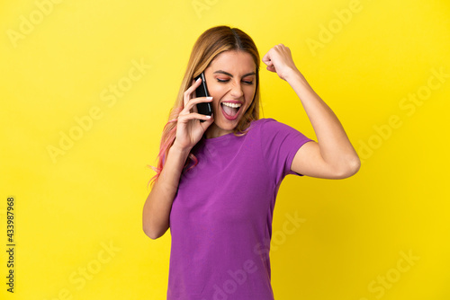 Young woman using mobile phone over isolated yellow background celebrating a victory © luismolinero
