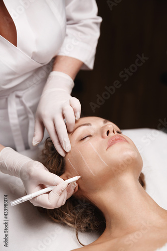 Spa and beauty clinic. Cosmetologist doctor making marks on client face with medical marker, skin preparation for cosmetology ultrasound lifting procedure, doctor using pencil for HUFU therapy