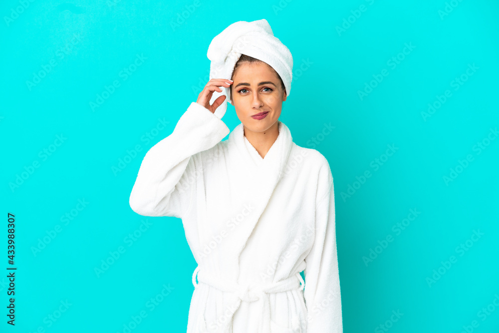Young woman in a bathrobe over isolated blue background having doubts