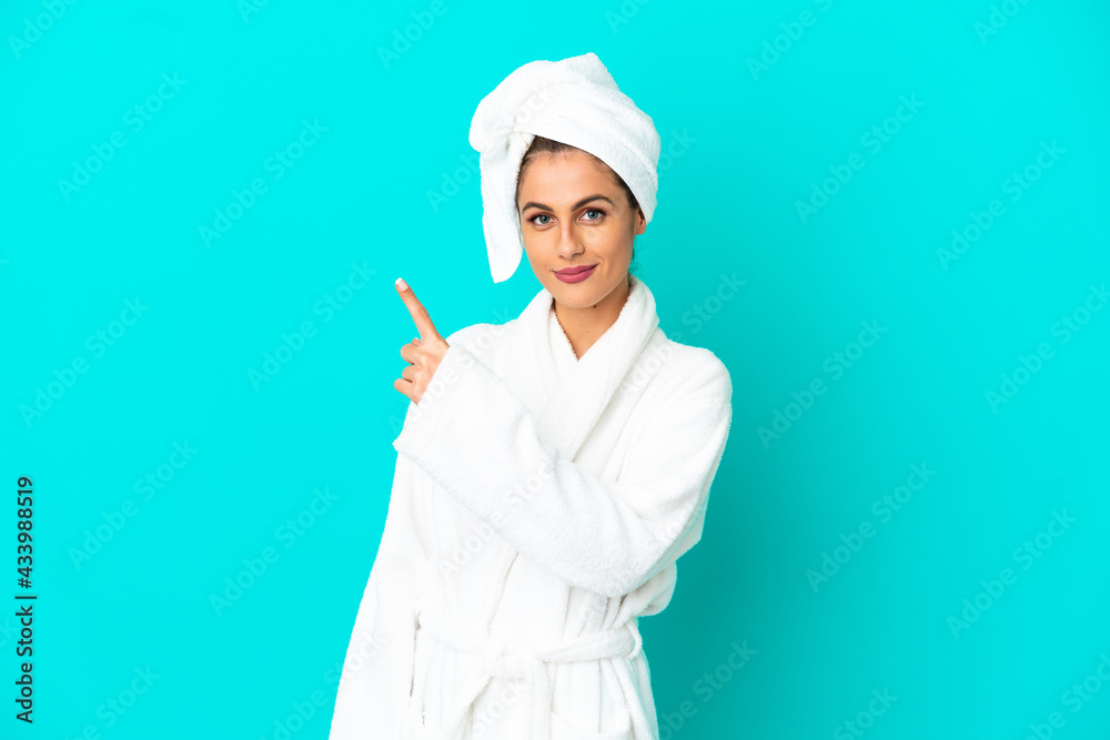 Young woman in a bathrobe over isolated blue background pointing to the side to present a product Young woman in a bathrobe over isolated blue background pointing to the side to present a product