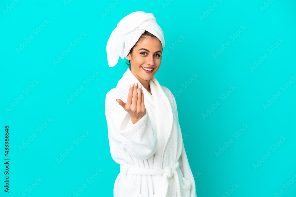 Young woman in a bathrobe over isolated blue background inviting to come with hand. Happy that you came Young woman in a bathrobe over isolated blue background inviting to come with hand. Happy that you came