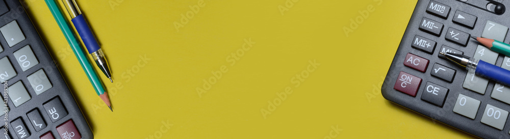 calculator pencil and pen on a yellow background. close-up. long banner. calculator pencil and pen on a yellow background. close-up. long banner.