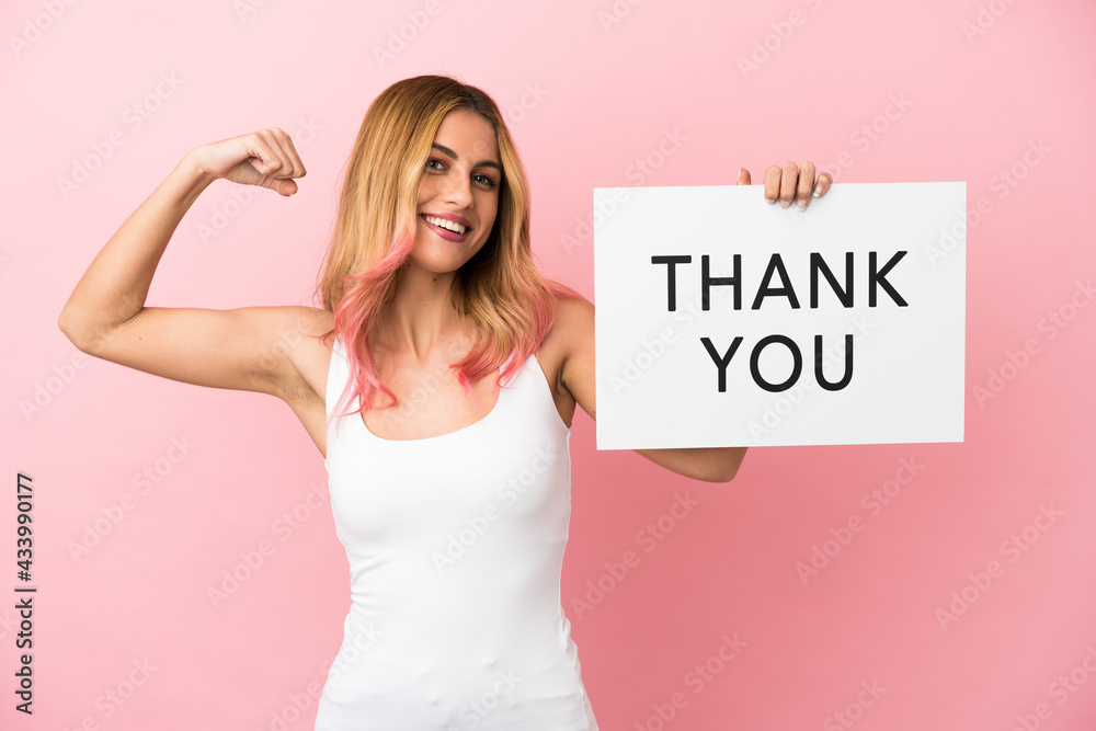 Young woman over isolated pink background holding a placard with text THANK YOU and doing strong gesture Young woman over isolated pink background holding a placard with text THANK YOU and doing strong gesture