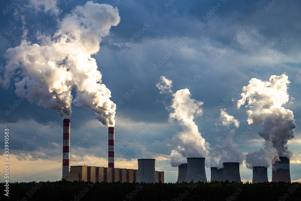 A view of the smoking chimneys of a coal-fired power plant against the backdrop of a dramatic sky with clouds. The photo was taken in natural daylight.