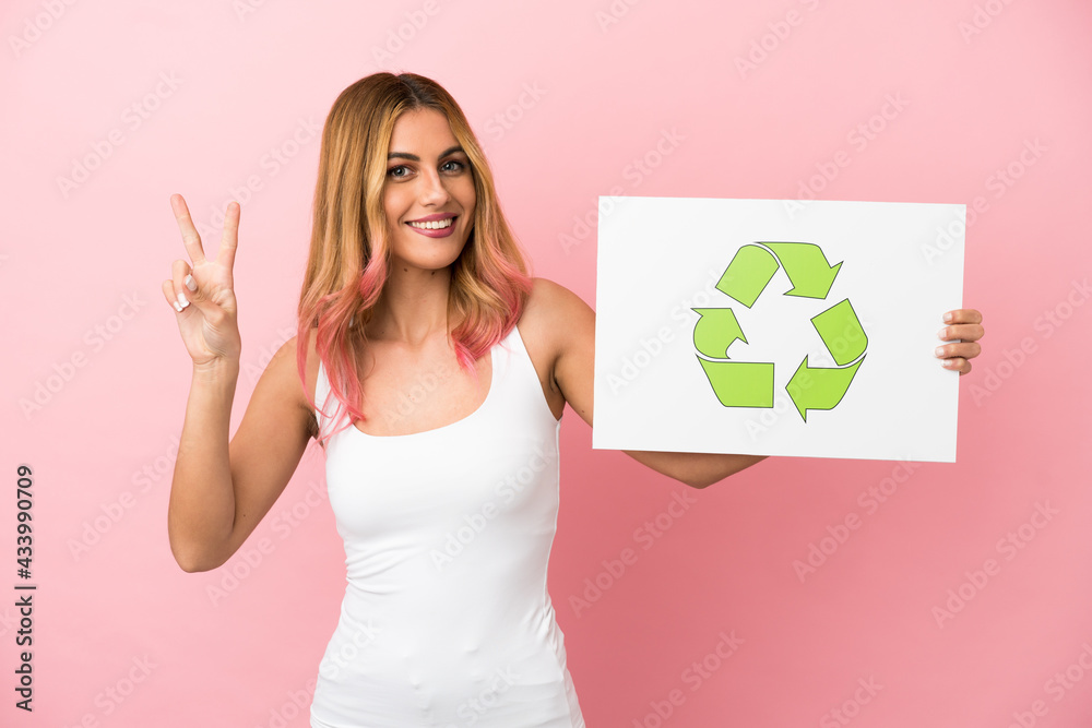 Young woman over isolated pink background holding a placard with recycle icon and celebrating a victory Young woman over isolated pink background holding a placard with recycle icon and celebrating a victory