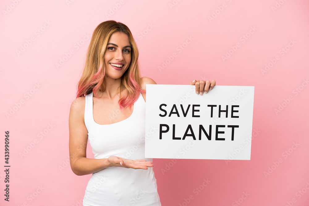 Young woman over isolated pink background holding a placard with text Save the Planet and pointing it Young woman over isolated pink background holding a placard with text Save the Planet and pointing it