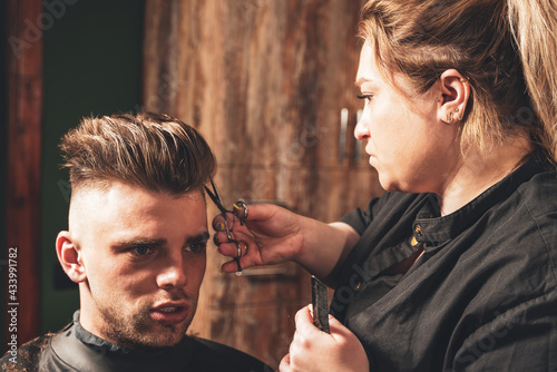 Girl hairdresser doing hairstyle and styling with scissors and comb to a young man