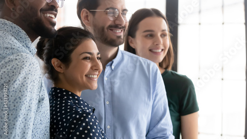 Millennial workers of different races celebrating accomplished project. Diverse happy employees standing together. Indian female business leader smiling and posing with colleagues. Candid shot