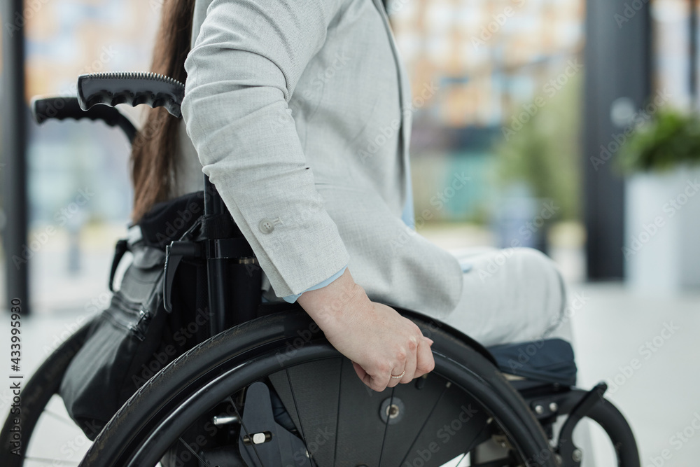 Obraz premium Close up of unrecognizable young businesswoman in wheelchair entering office building or school, copy space