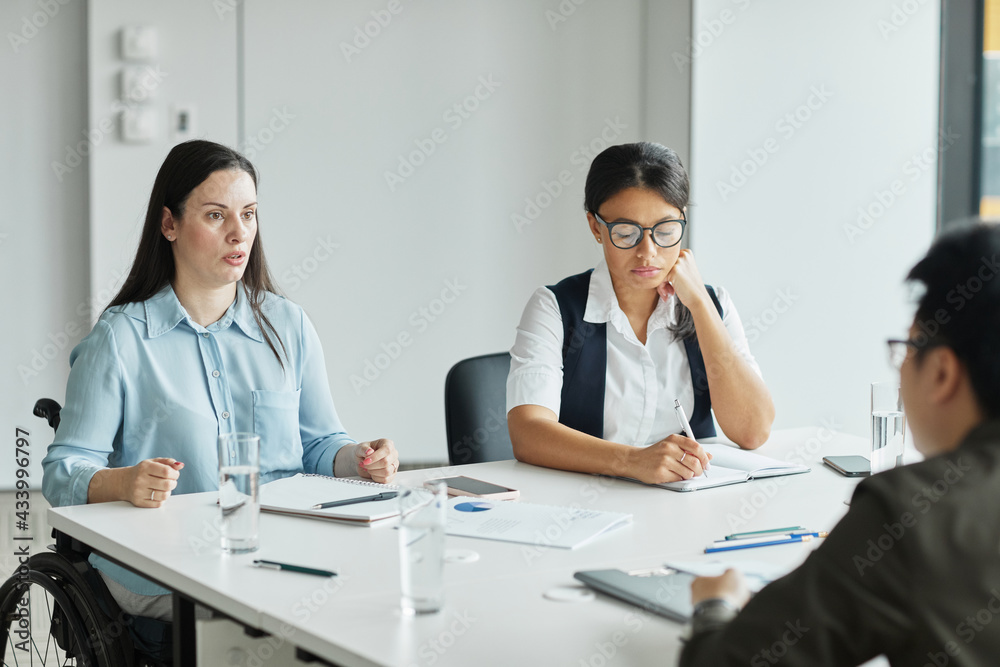 Diverse business team discussing project at table in modern office with focus on young woman in wheelchair sharing ideas Diverse business team discussing project at table in modern office with focus on young woman in wheelchair sharing ideas