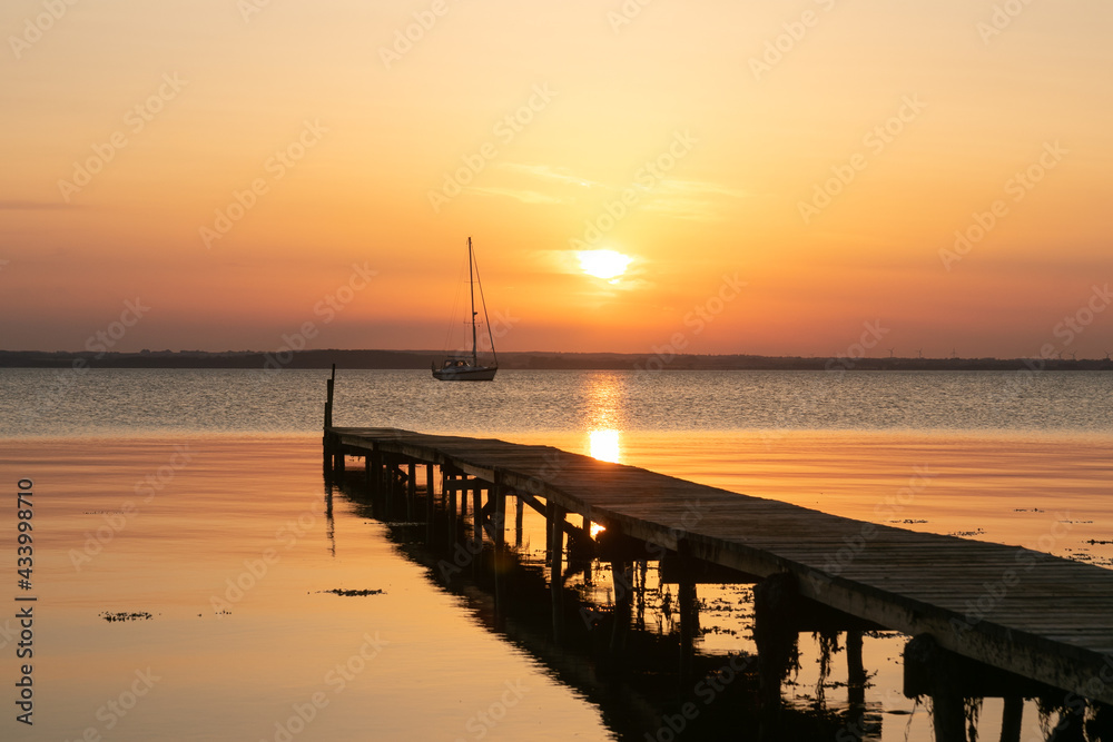 Steg und Segelboot bei Sonnenuntergang