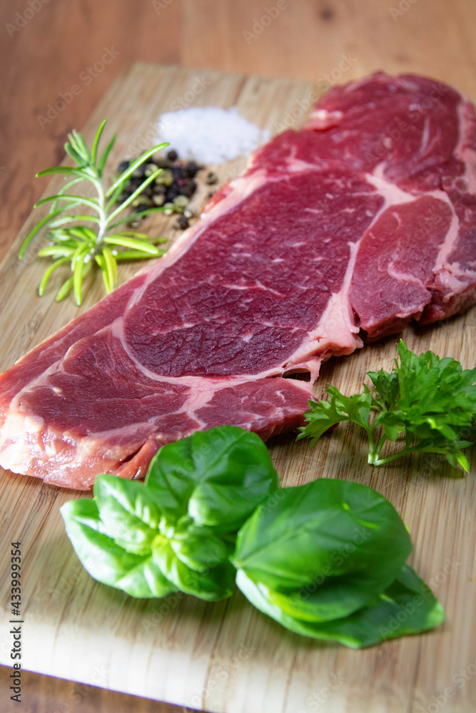Raw entrecote steak with salt, pepper, basil, parsley and rosemary