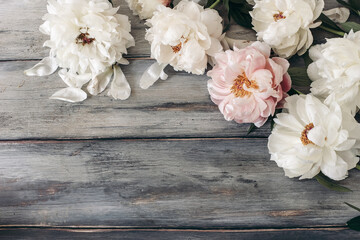 Decorative floral frame, banner made of pink and white peonies flowers. Old grey wooden table background. Empty copy space. Flat lay, top view. Picture for blog. Summer wedding or birthday concept.