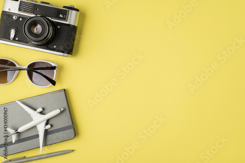 Top view photo of camera sunglasses pen and plane model on grey notebook on isolated pastel yellow background with copyspace