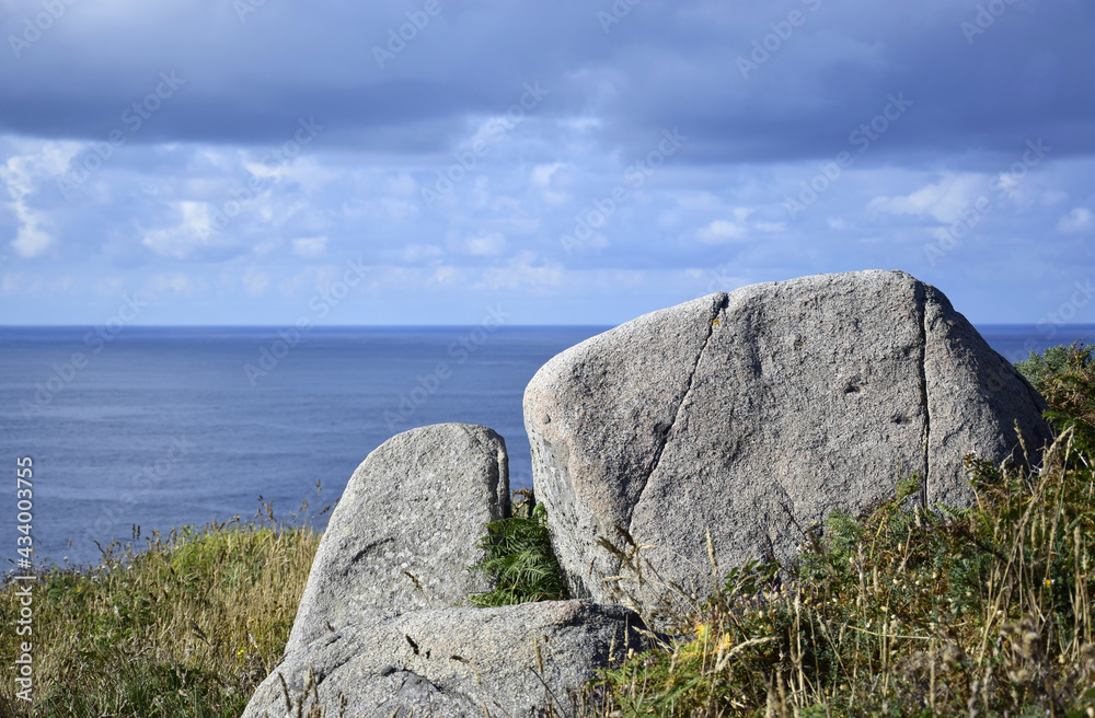 A rock on a cliff with the sea and the clouds in the background