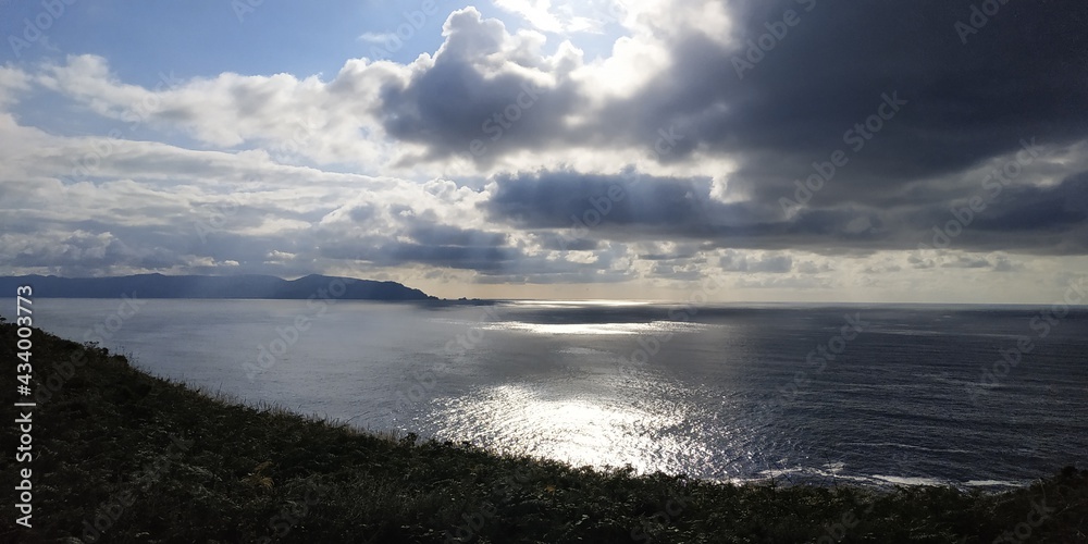 The sun's rays pass through the clouds and light up the sea in a coastal landscape