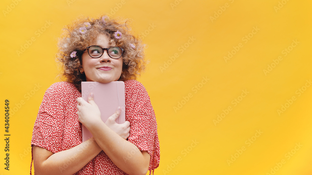 Naklejka premium Excited young woman student or writer holding book and thinking. Curly hair full of spring flowers. High quality photo