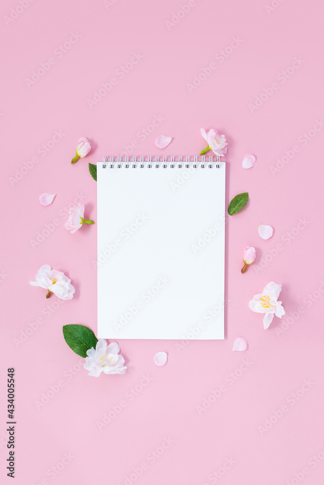 The blank notebook is decorated with spring sakura flowers on pink background. Springtime concept. Template for designers. Flat lay.