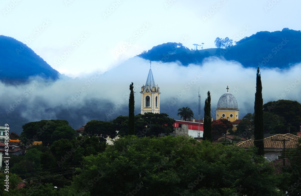 Large image of a beautiful misty mountain landscape in a small town called Joanopolis in the countryside of Brazil. Catholic church clock and bell tower view among foggy mountains and stunning nature Large image of a beautiful misty mountain landscape in a small town called Joanopolis in the countryside of Brazil. Catholic church clock and bell tower view among foggy mountains and stunning nature