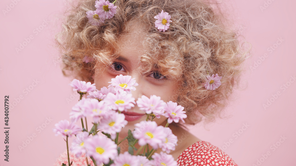 Naklejka premium Happy young woman smelling bouquet of spring roses. Portrait of caucasian girl with flowers in her curly hair . High quality photo