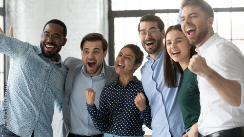 Multiethnic team of excited employees celebrating corporate achievement, high sales result, work success, shouting for joy. Happy diverse professionals hugging, laughing, making winner gestures