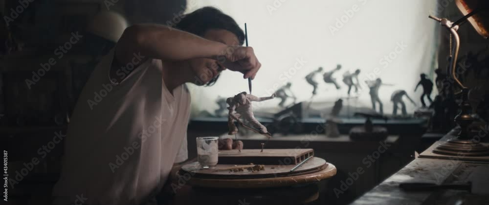 Artist apply glaze on sculpture paintbrush in hand in dark atelier