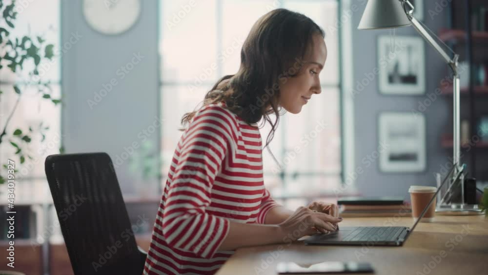 Young Woman Using Laptop at Home for Remote Work. Beautiful Young Brunette Girl Sitting at Her Desk Uses Internet, Doing Productive Distant Work. Side View Medium Arc Shot