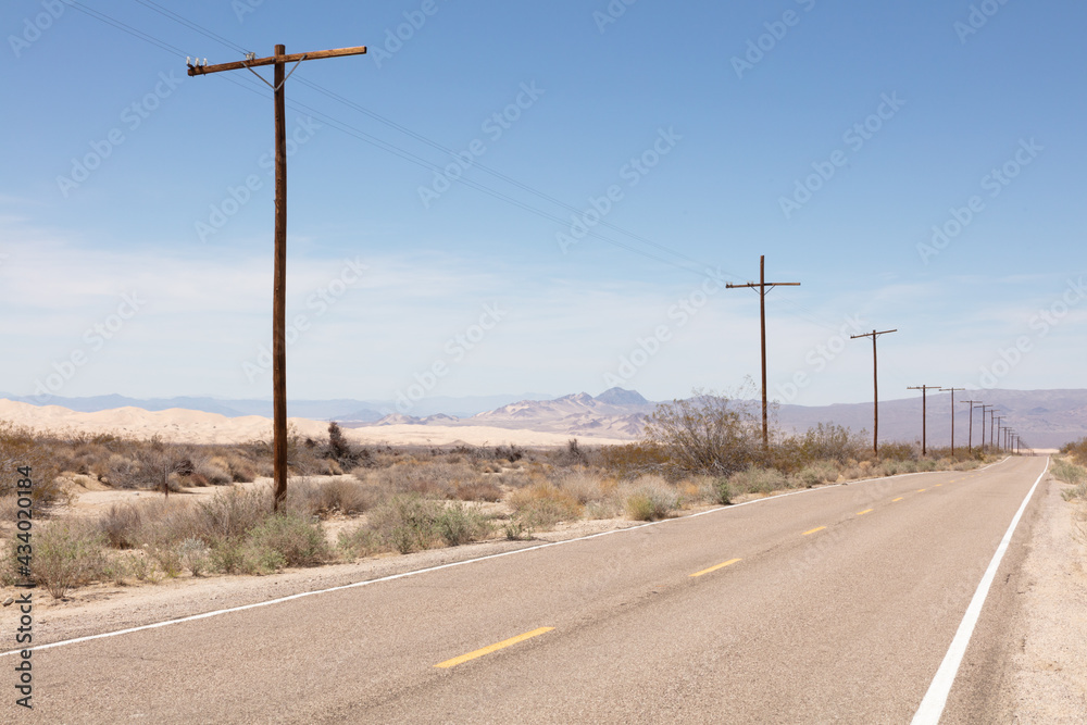 row of telephone poles along a road crossing the Mojave Desert under a blue sky