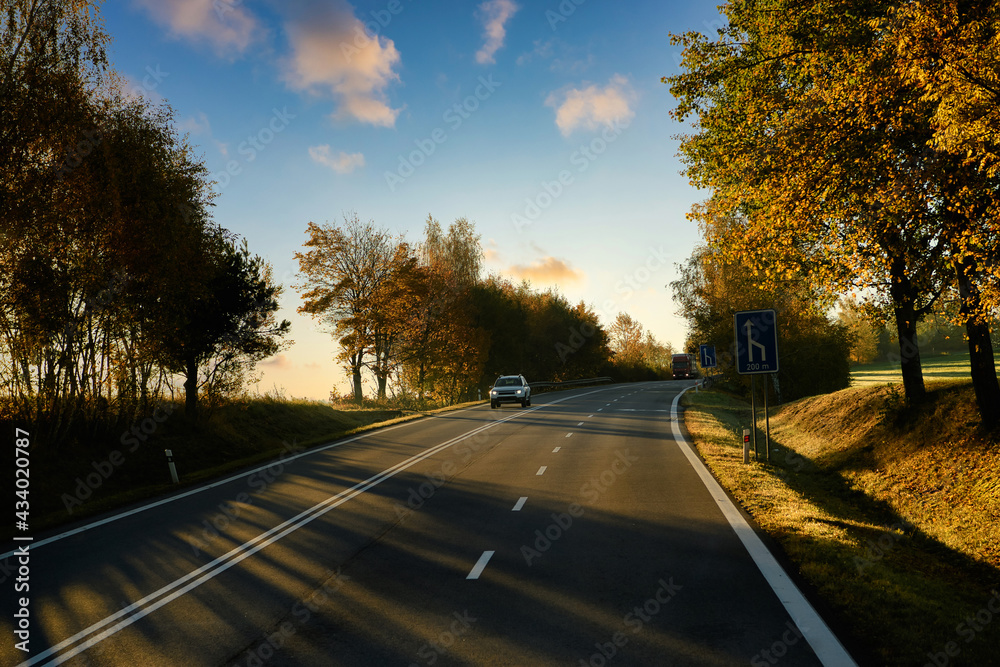 Fototapeta premium Travel with beautiful European driving routes, highways and cars and both sides with big trees changing color in autumn, rural views and evening lights create a romantic atmosphere.