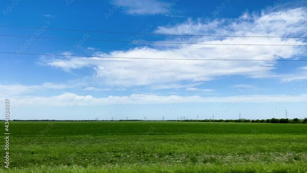 Ein grünes Feld im vorbeifahren, mit kleinen Strommasten, blauem Himmel und weißen Wolken Ein grünes Feld im vorbeifahren, mit kleinen Strommasten, blauem Himmel und weißen Wolken