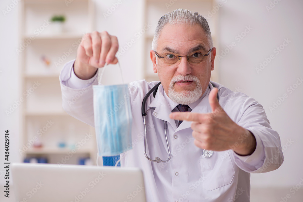 Old male doctor working in the clinic during pandemic Old male doctor working in the clinic during pandemic