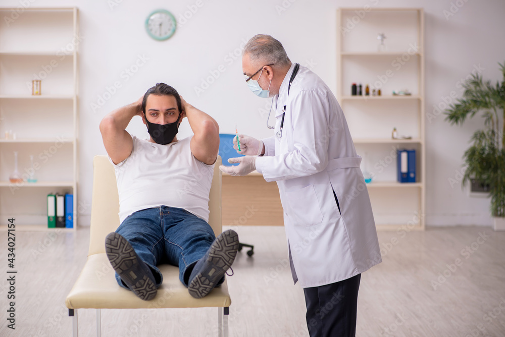 Young male patient visiting old doctor in vaccination concept Young male patient visiting old doctor in vaccination concept
