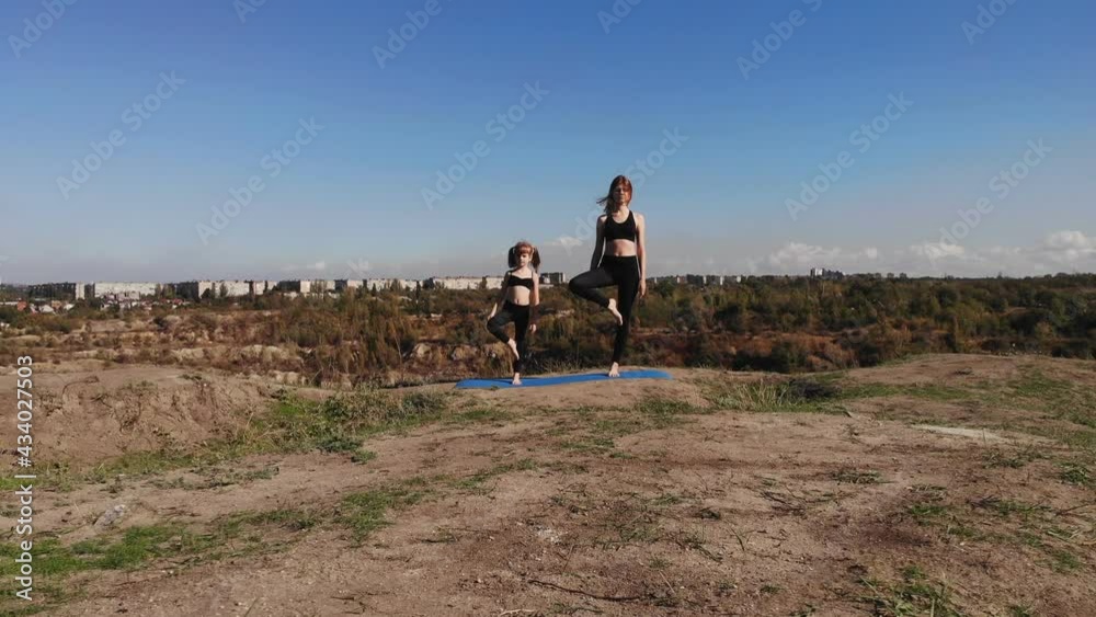 Family pilates training together. Young mother and her child daughter do stretching exercises on top of hill in sunny morning. Sport education and kids development Family pilates training together. Young mother and her child daughter do stretching exercises on top of hill in sunny morning. Sport education and kids development