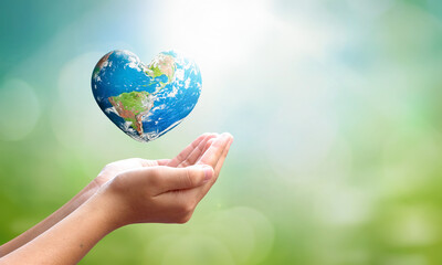 World environment day concept: man opens palms and drags heart shaped earth globe over blurred blue sky and water background. Elements of this image furnished by NASA