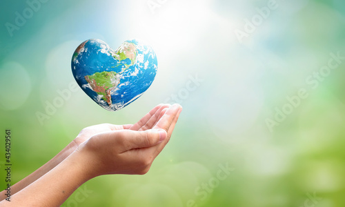 World environment day concept: man opens palms and drags heart shaped earth globe over blurred blue sky and water background. Elements of this image furnished by NASA