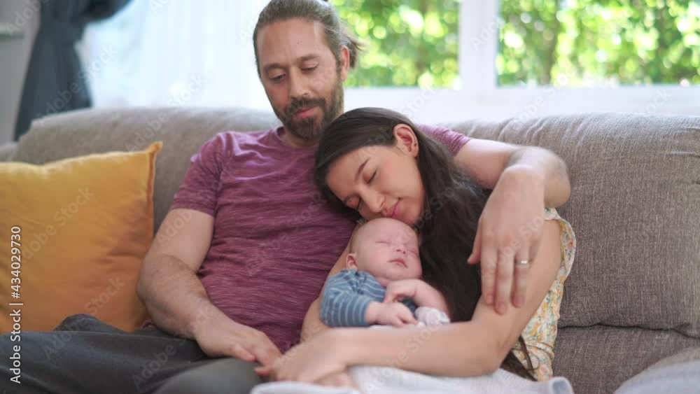 Caucasian man caring sleeping wife and adorable newborn baby son on sofa in living room. Family spending time together at home. Family bonding relationship and newborn baby healthcare concept. Caucasian man caring sleeping wife and adorable newborn baby son on sofa in living room. Family spending time together at home. Family bonding relationship and newborn baby healthcare concept.